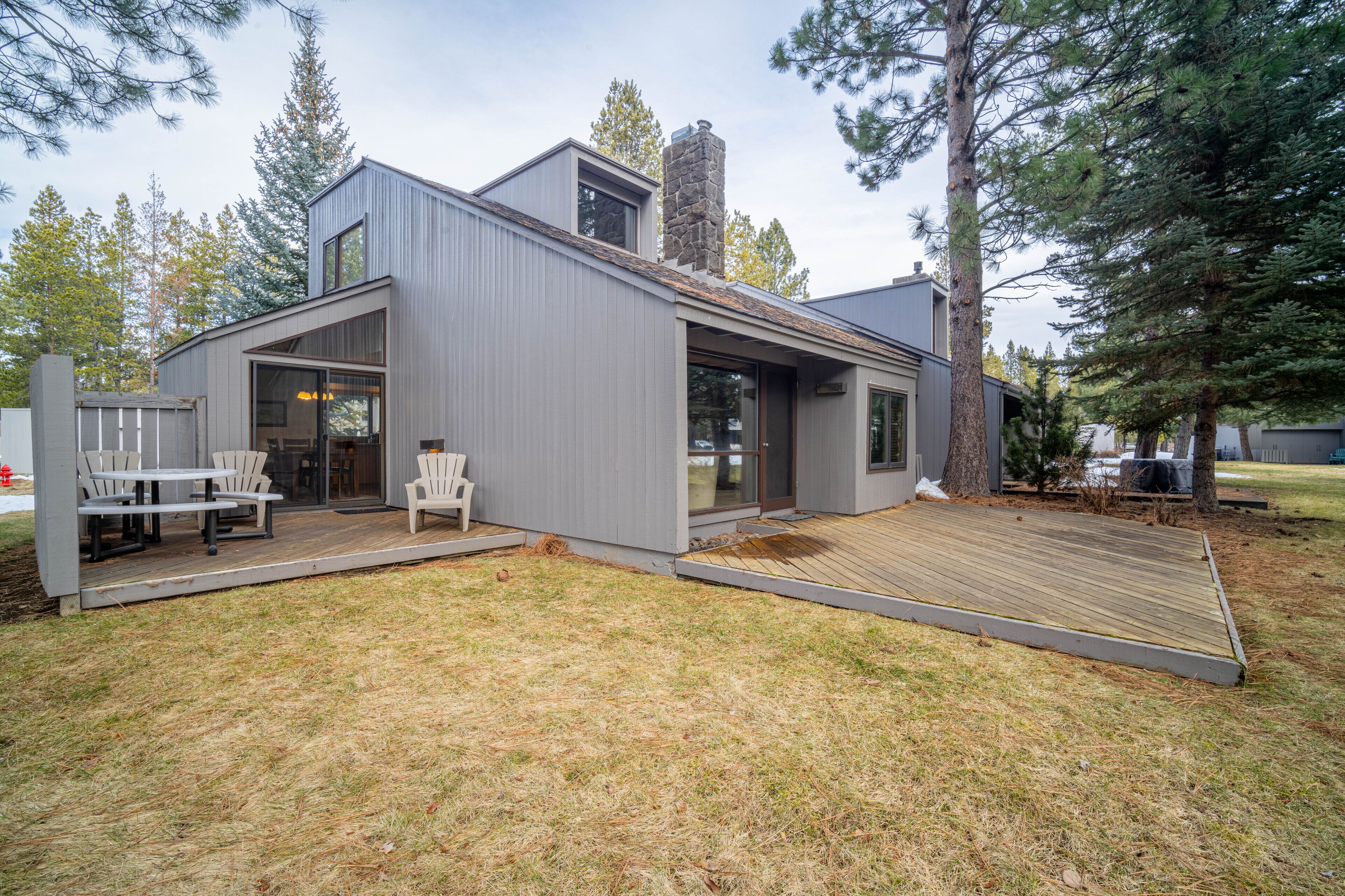 A modern house with a deck, a stone chimney, and a large glass door.
