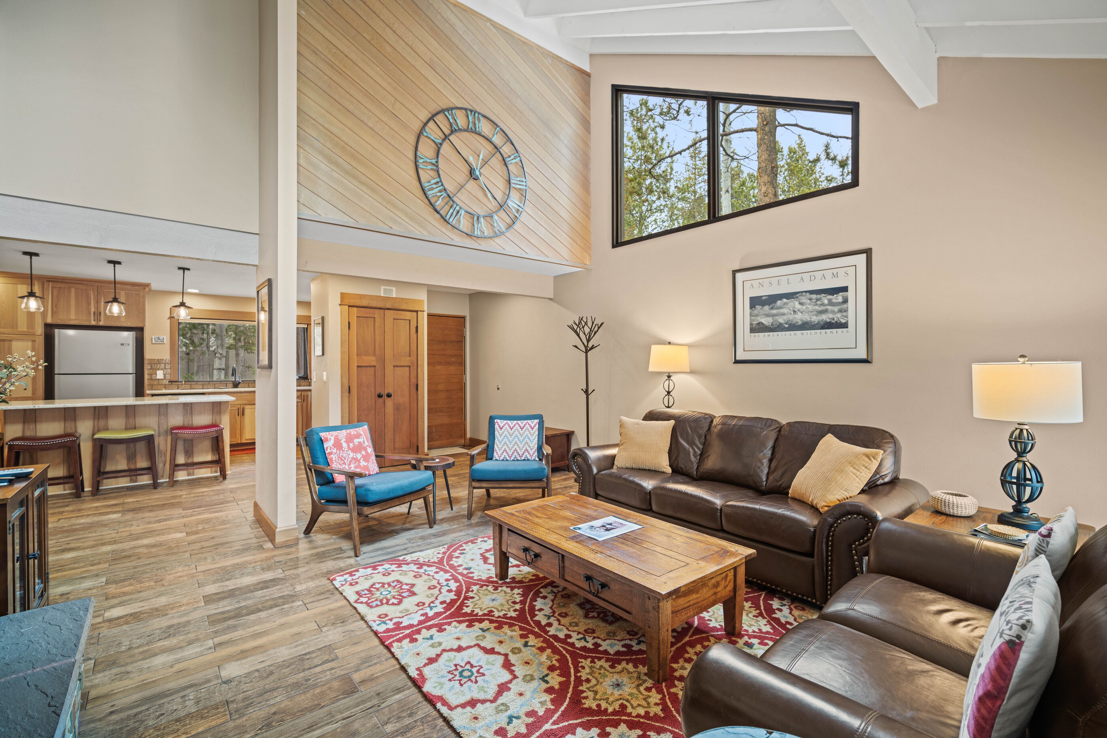 A spacious living area with a large wooden ceiling, a dining area with bar stools, and a kitchen with a refrigerator.