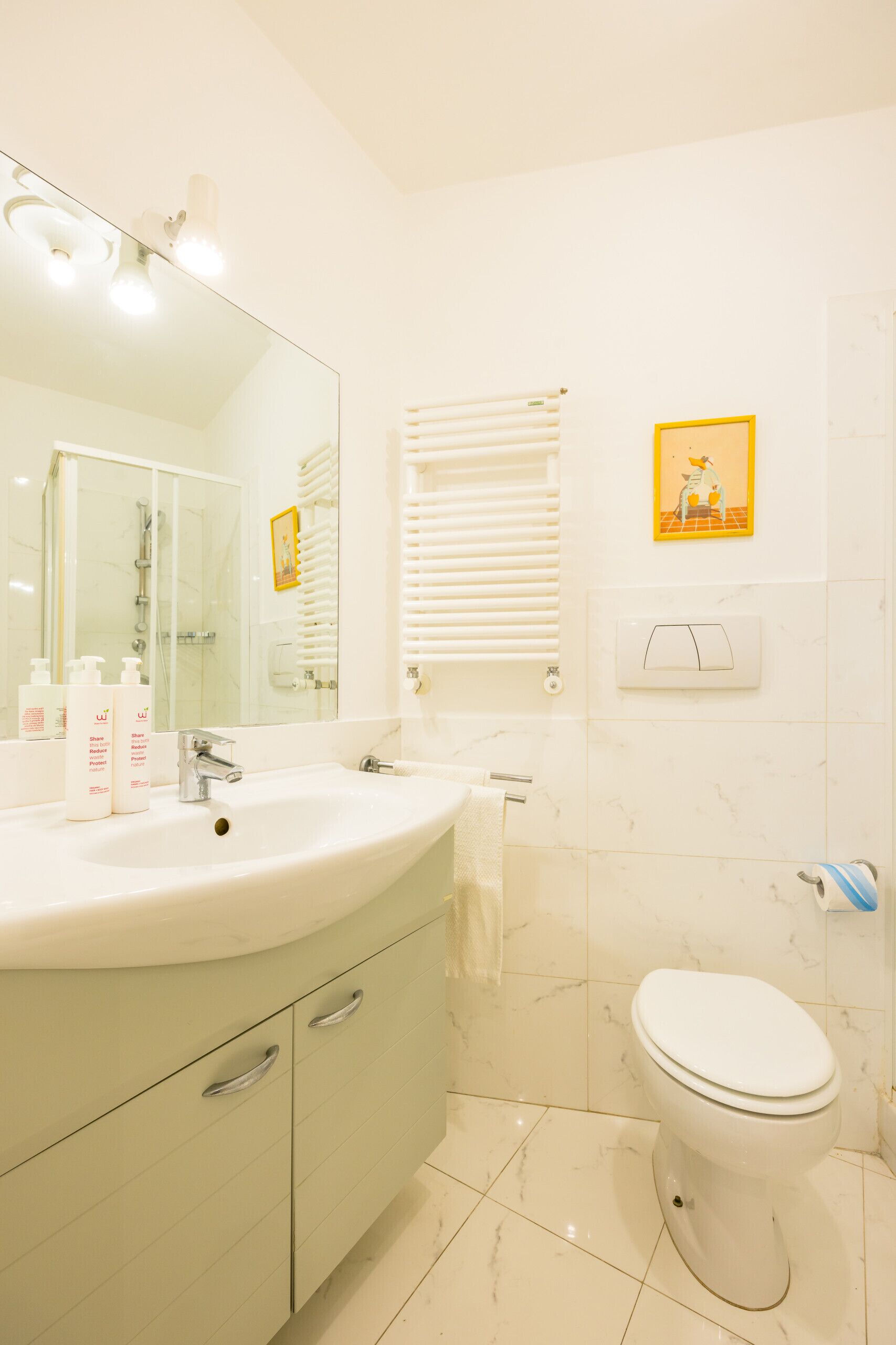 Un bagno con lavandino, specchio, WC e portasciugamani.