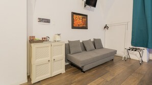 Een kamer met een bank, een kast, een aan de muur bevestigde televisie en een raam met gordijn.