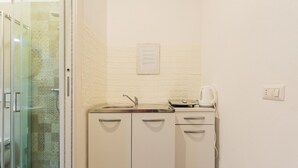 Een kleine keuken met een gootsteen, waterkoker en kastje.