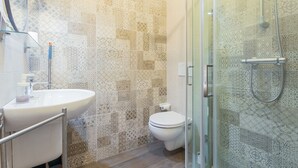 Een badkamer met patroon betegelde vloeren, een witte wastafel en een douche met glazen wanden.