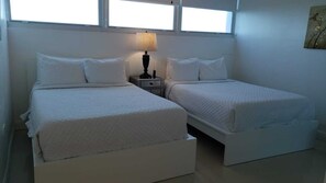 Ein Zimmer mit zwei Betten, einem Nachttisch mit Lampe und einem Fenster.