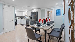 Una cocina moderna con armarios blancos, un refrigerador de acero inoxidable y un comedor con mesa preparada para cuatro.