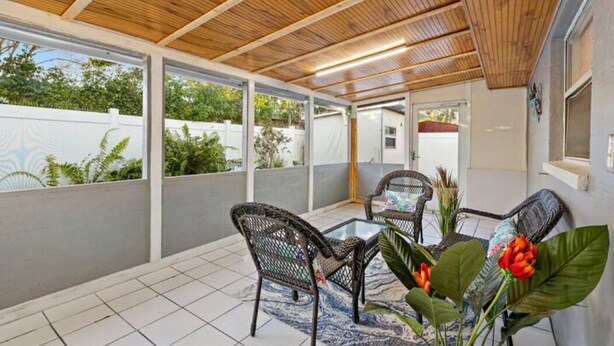 Un patio al aire libre con techo de madera, suelo de baldosas y mobiliario de mimbre.