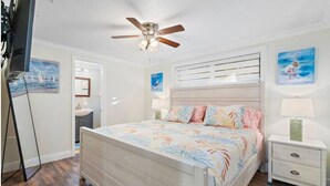 Un dormitorio con cama de madera, ventilador de techo, mesita de noche y decoración en la pared.