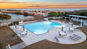 A rectangular pool with a white deck, surrounded by lounge chairs and tables, with a view of the ocean and beach at sunset. - Golf Cart | Near Private Beach Access (Watersound)
