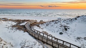 A snow-covered beach with a wooden boardwalk leading to a small structure. - Golf Cart | Near Private Beach Access (Watersound)