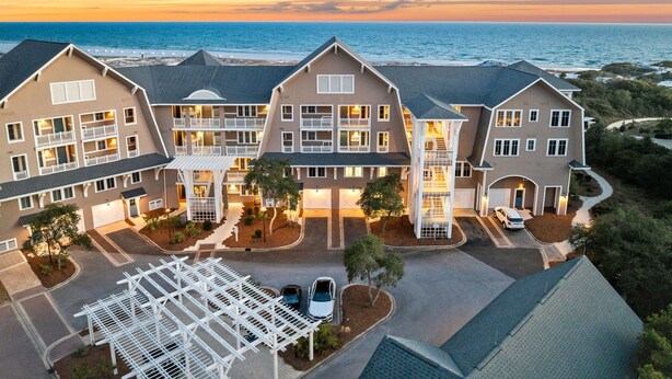 A multi-story hotel with balconies overlooking a beach, a covered parking area, and a clear view of the ocean at sunset. - Golf Cart | Near Private Beach Access (Watersound)