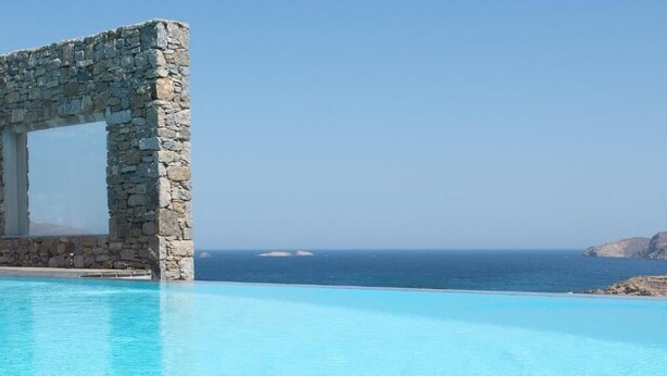 Struttura ad arco in pietra sopra una piscina cristallina, con vista sul mare e isole in lontananza.