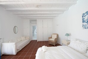 Une pièce blanche avec un lit, une chaise, une table de chevet et une armoire.