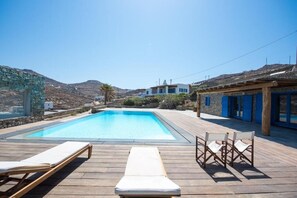 Une piscine avec des chaises longues, une terrasse en bois et un mur en pierre.