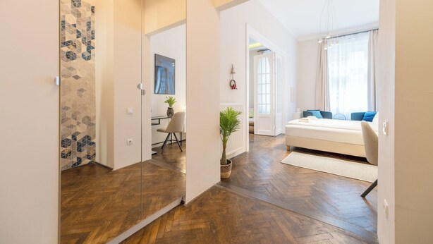 A modern interior with a wooden floor, a white sofa, and a dining area with a table and chairs. - Venus Apartments - Opera III (Budapest)