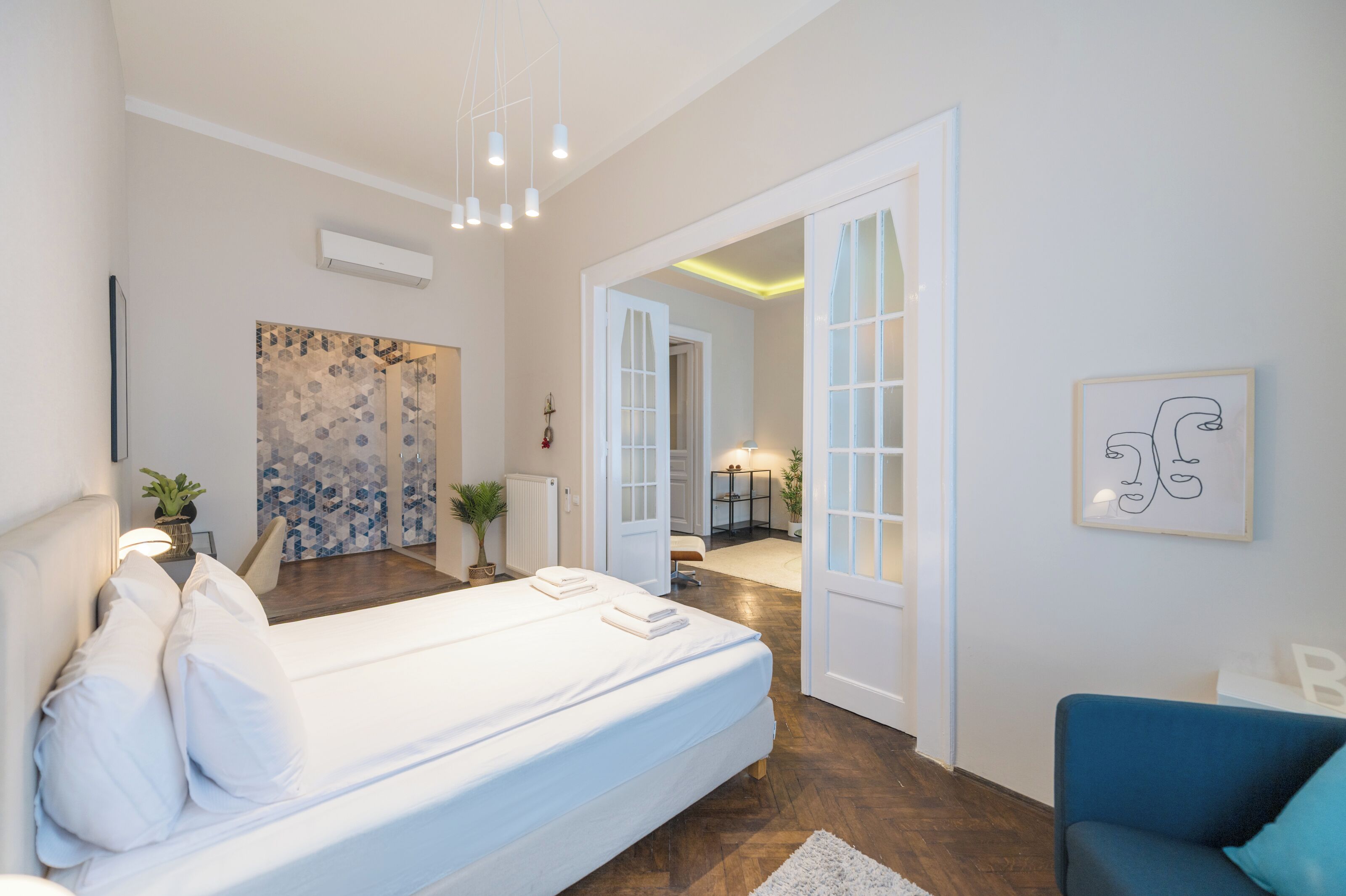 Ein modernes Schlafzimmer mit einem großen Bett, einem blauen Sessel und Blick ins Bad.