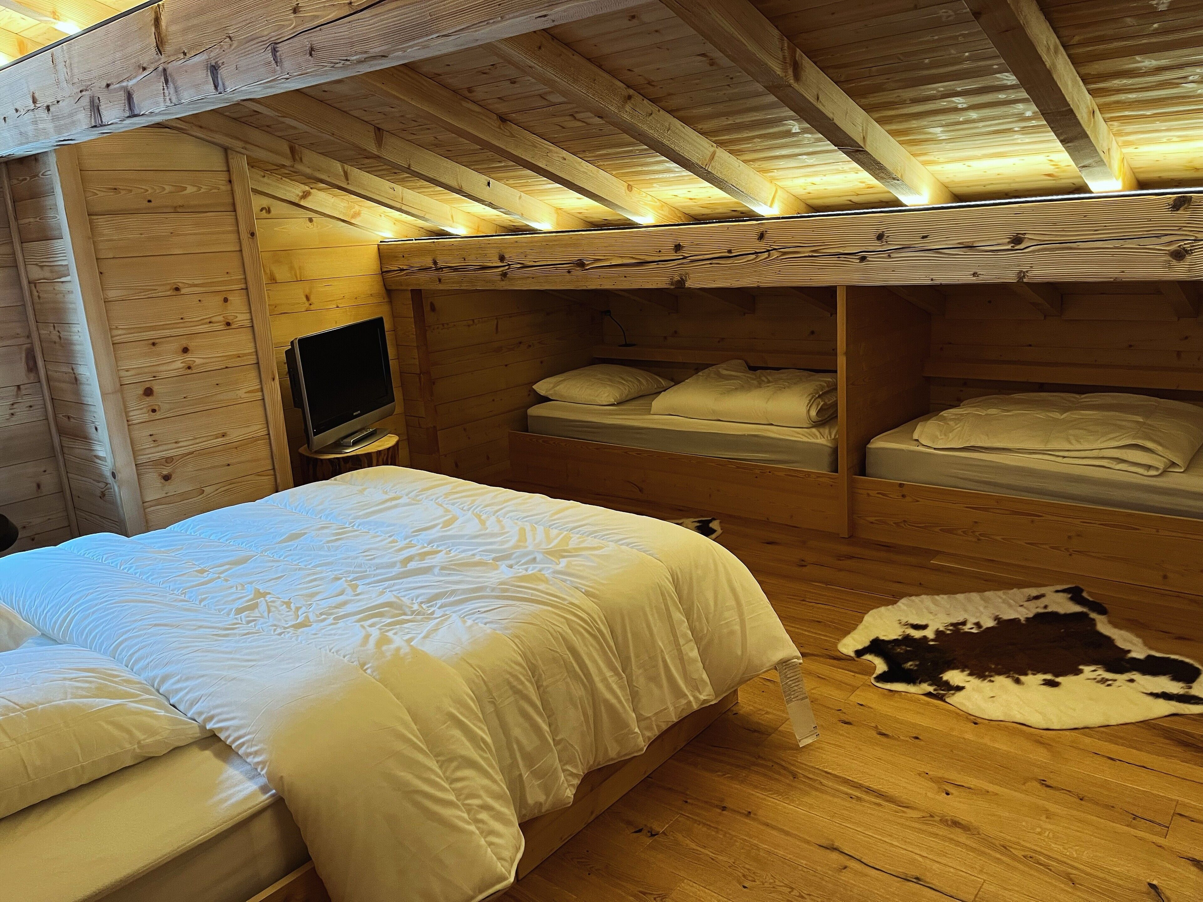 Une chambre de style rustique, avec un lit simple, une télévision et un tapis en peau de vache sur le plancher en bois.