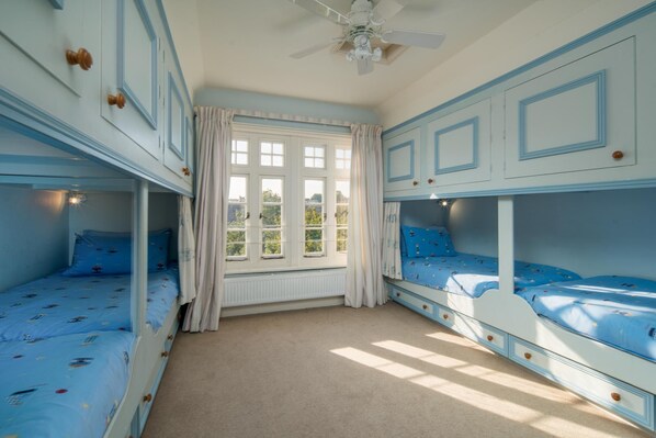 A room with bunk beds, a ceiling fan, and a window with curtains.
