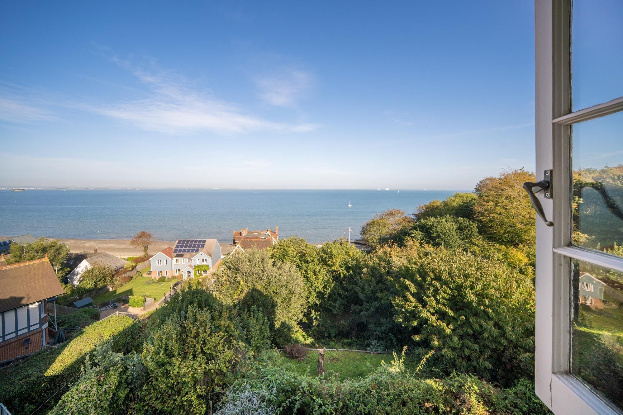 A coastal view from a window overlooking a beach, houses, and dense greenery.