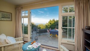 A room with a glass door leading to an outdoor seating area with a table, chairs, and a view of the sea.