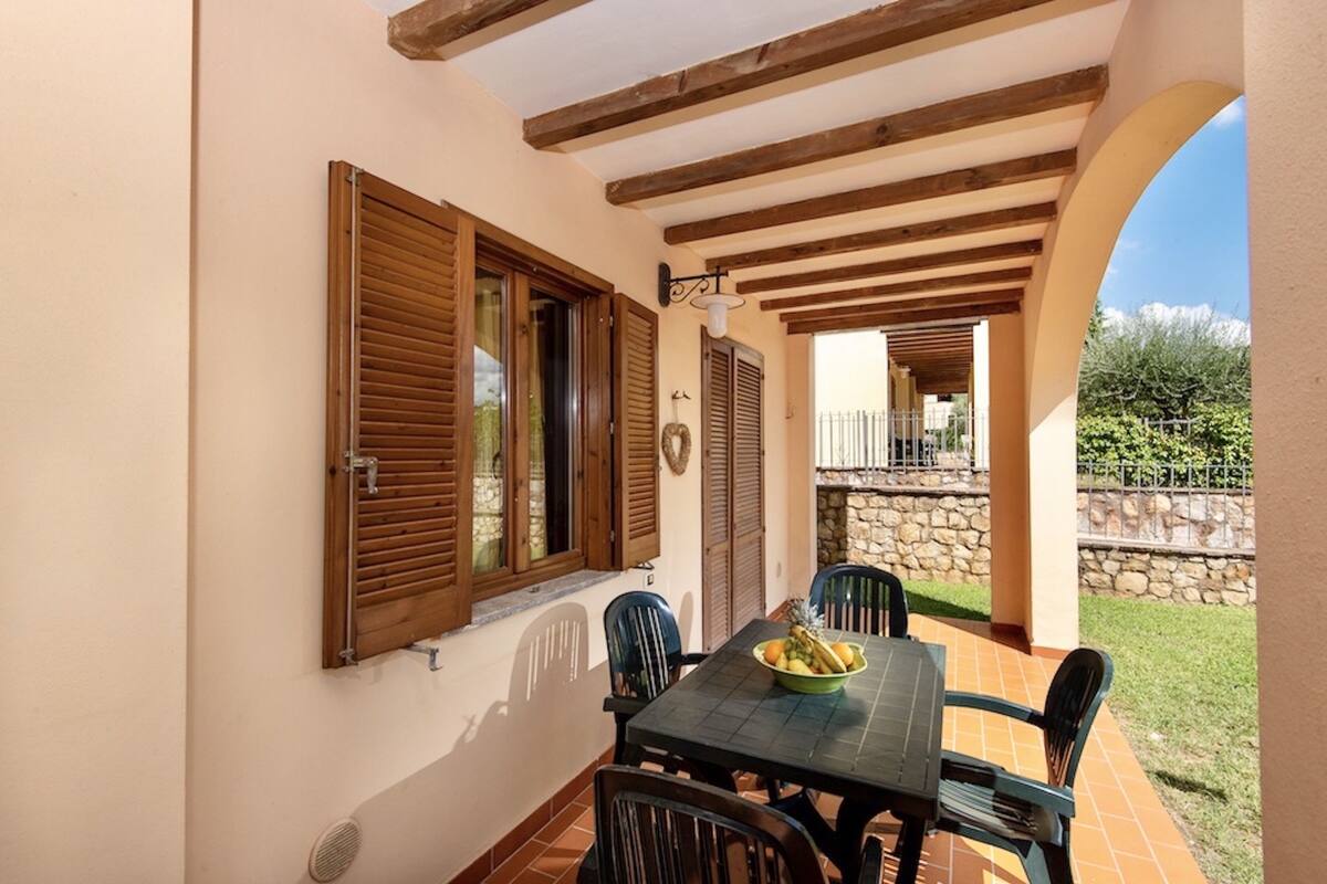 A covered patio with a table and chairs, a stone wall, and a view of the garden.