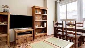 Una sala de estar con televisor, muebles de madera, una estantería y una zona de comedor con sillas y mesa.
