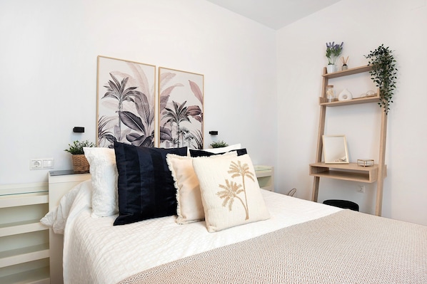 Une chambre à coucher bien rangée, avec un lit, des oreillers, une table de chevet, une étagère murale agrémentée de plantes et un tableau encadré.