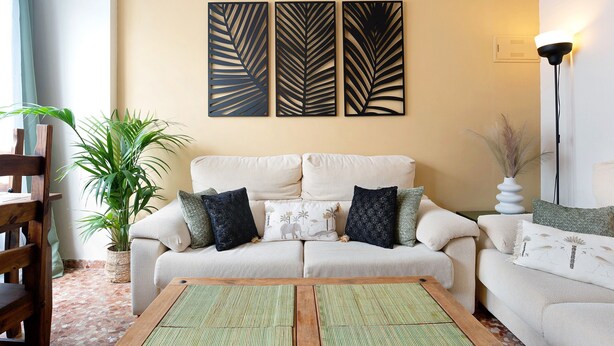 Una sala de estar con un sofá, una mesa de centro, una planta en maceta y decoración en la pared.