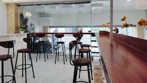 Eine moderne Bar mit einer langen Theke, mehreren Hockern und einer Glastrennwand.