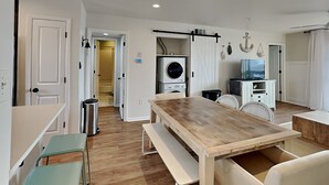 A modern kitchen with a wooden table, a built-in washing machine, and a dining area with chairs. - Lighthouse Point 7C | Easy Access to Pool & Beach! (Tybee Island)