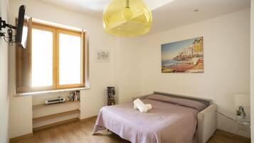 A bedroom with a bed, a window, a painting, and a lamp.