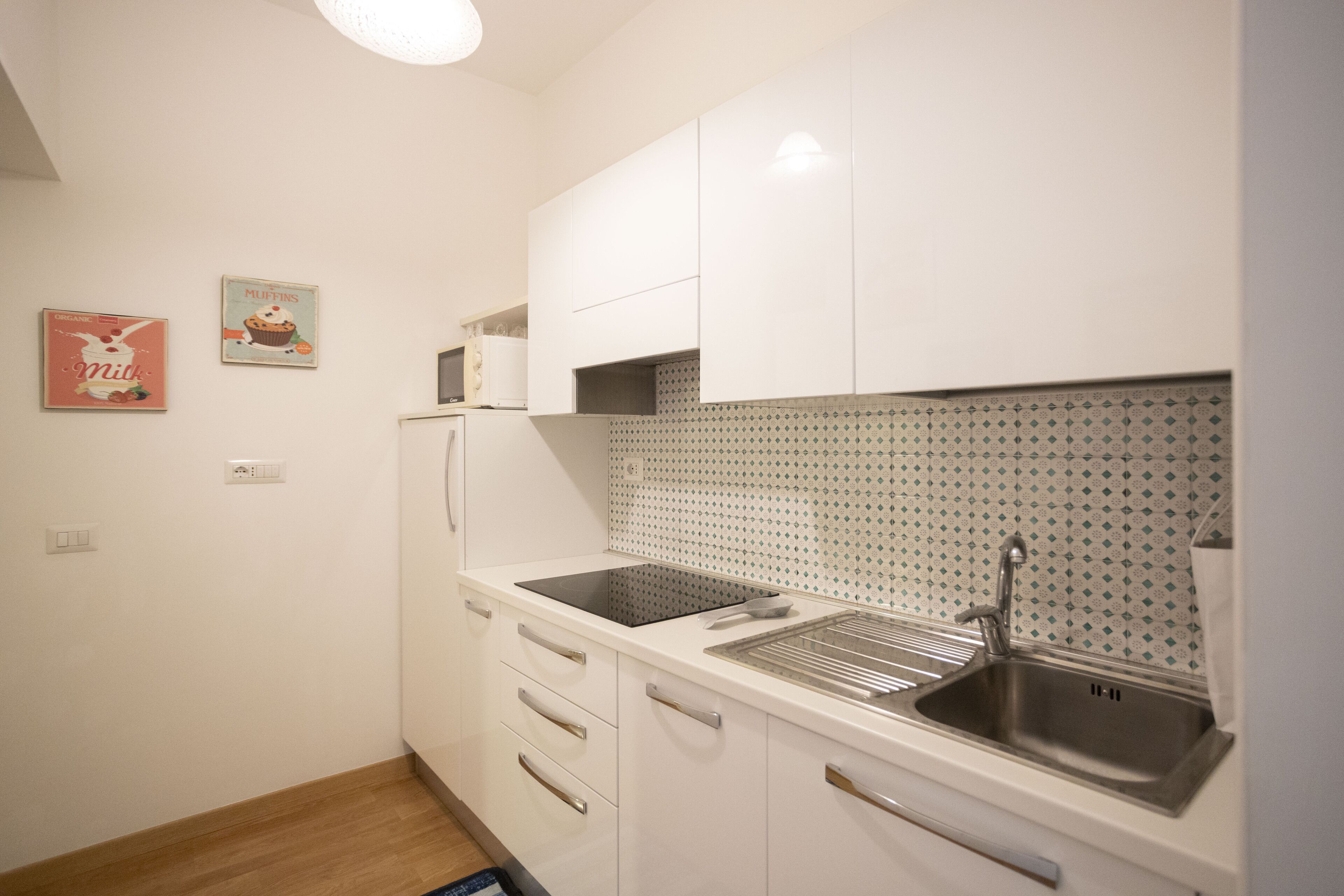 Cocina compacta con armarios blancos, cocina por inducción negra y pileta de acero inoxidable.