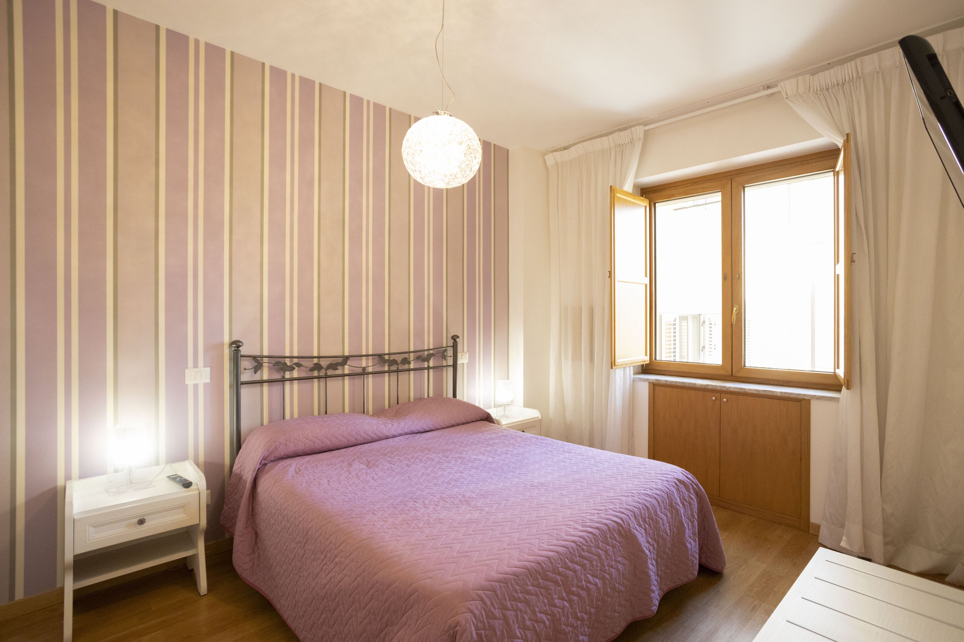 Quarto com cama, mesa de cabeceira, janela e cortina.