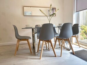 Un espace repas moderne avec une table en verre, quatre chaises et un vase rempli de fleurs.