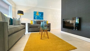 Ein modernes Wohnzimmer mit einem grauen Sofa, einem gelben Teppich, einem Glastisch und einem Bild an der Wand.