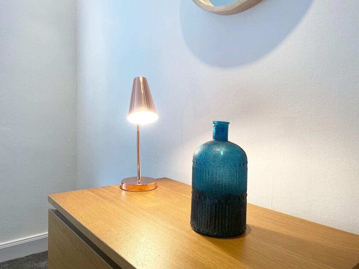 Una mesita de noche de madera con un jarrón azul y una lámpara.