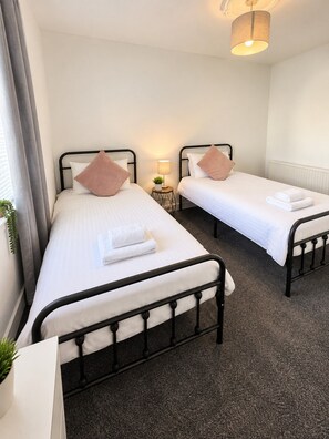 A hotel room with two single beds, a small bedside table with a lamp, and a radiator. - Trident Apartment - newly renovated bright and airy flat located in a very convenient central area. (Paisley)