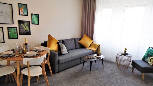 Una sala de estar con un sofá gris, una mesa redonda de centro, una mesa de comedor lista para cuatro comensales y una pequeña mesita auxiliar.