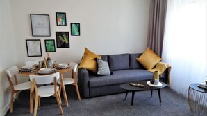 Una sala de estar con un sofá gris, dos cojines amarillos, una mesita de centro y una zona de comedor con una mesa dispuesta para dos personas.