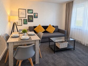 A living room with a sofa, a dining table set with plates, a lamp, and framed pictures on the wall.