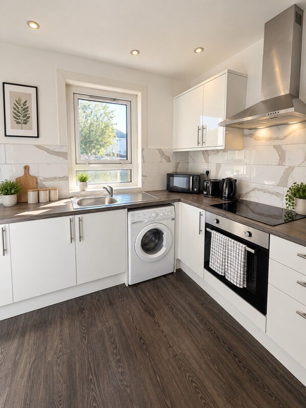 A modern kitchen with white cabinetry, a built-in washing machine, a microwave, and an oven.