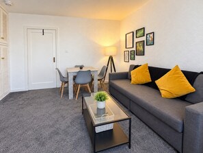 A living room with a sofa, a coffee table, a dining table with chairs, and a lamp. - Trident Apartment - newly renovated bright and airy flat located in a very convenient central area. (Paisley)