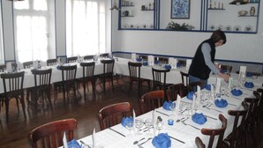 A dining area with multiple tables set for service, a person attending to the tables, and a wall with decorative items and a framed picture. - Hôtel Magne (Saurier)