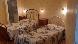 A bedroom with two single beds, a wooden nightstand, a dresser, and a mirror. - Hôtel Magne (Saurier)