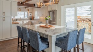 A modern kitchen with white cabinets, a marble island, and blue upholstered chairs. - Luxurious Mt CB Home | 5 Bedroom | Home Gym | Hot Tub | Gas Grill | Mtn Views (Mt. Crested Butte)