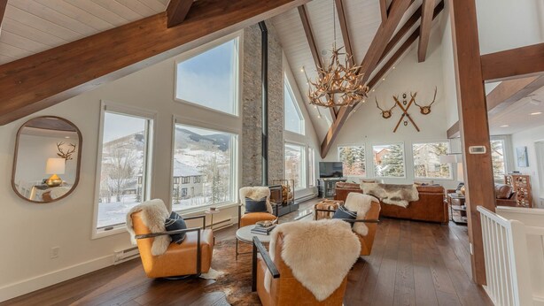 A spacious loft with high ceilings, large windows offering mountain views, and a rustic chandelier. - Luxurious Mt CB Home | 5 Bedroom | Home Gym | Hot Tub | Gas Grill | Mtn Views (Mt. Crested Butte)