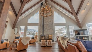 A spacious living room with a high ceiling, large windows, a fireplace, and leather furniture. - Luxurious Mt CB Home | 5 Bedroom | Home Gym | Hot Tub | Gas Grill | Mtn Views (Mt. Crested Butte)