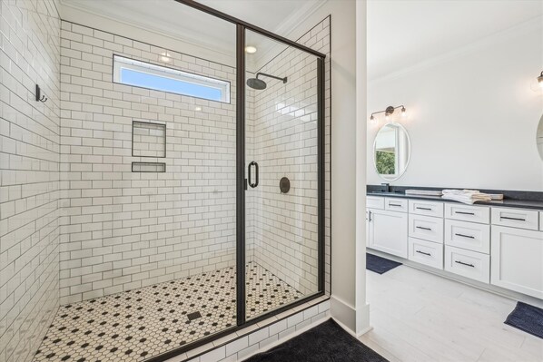 A modern bathroom with a glass-enclosed shower, white subway tiles, and a black and white patterned floor.
