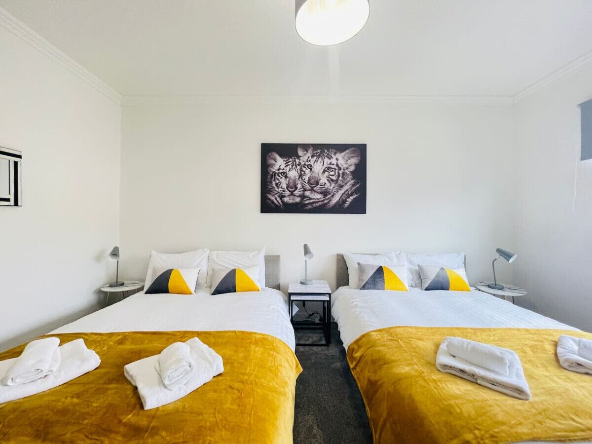 Een hotelkamer met twee bedden, elk voorzien van een gele sprei en witte kussens. Daarboven hangt een schilderij aan de muur en tussen de bedden staat een klein tafeltje met een lamp.