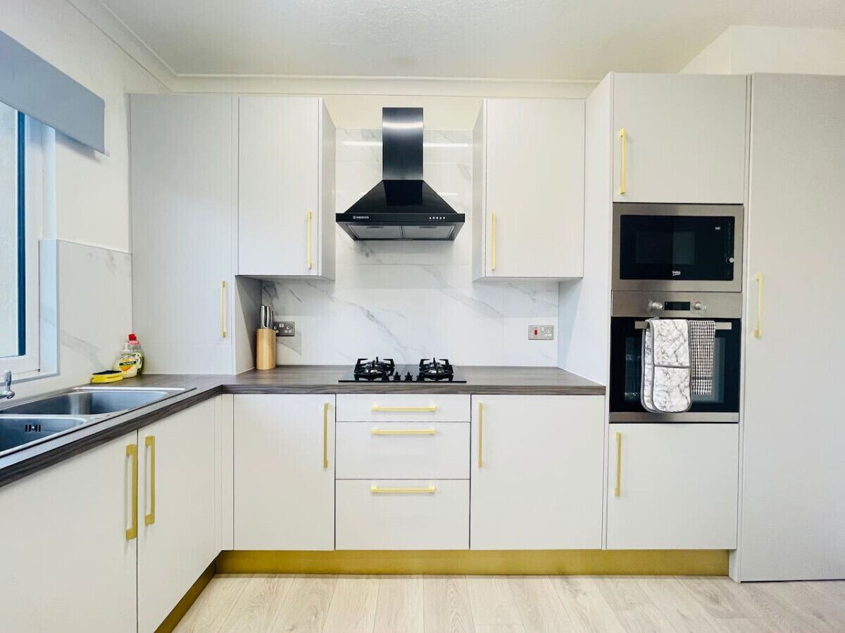 A modern kitchen with white cabinets, a black range hood, a microwave, and a gas stove.