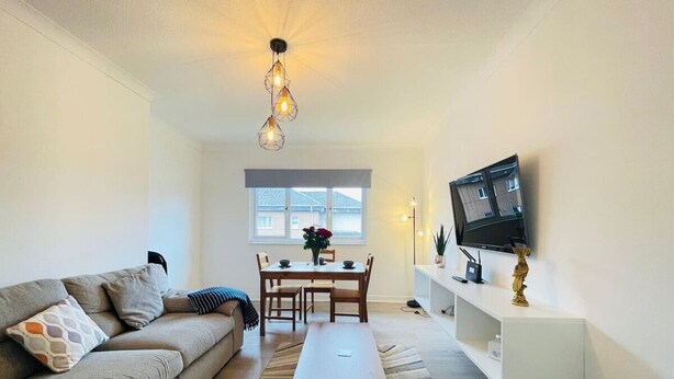 Ein Wohnzimmer mit Sofa, Couchtisch, Fernseher und einem Essbereich mit Stühlen und Tisch.