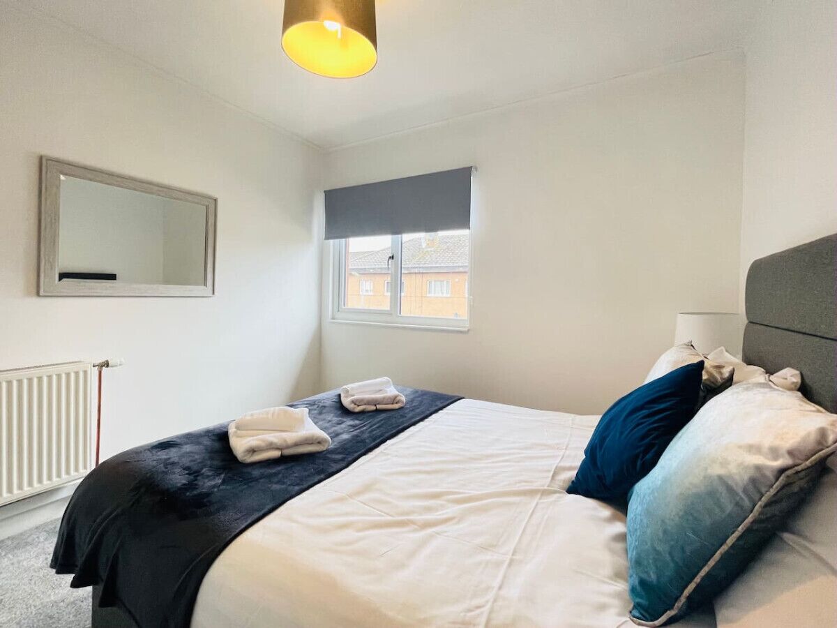 Een net opgemaakt bed met een donker hoofdbord, een raam met uitzicht op gebouwen en een spiegel aan de muur.